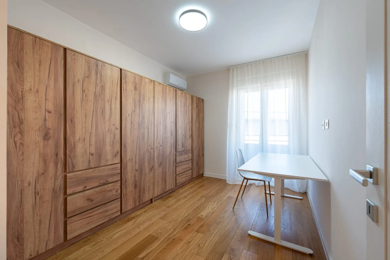 Small bedroom with a large wooden wardrobe, a desk, and a window.