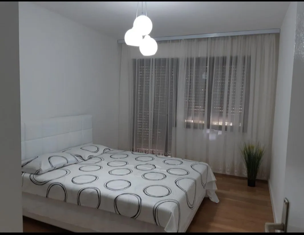 Svijetla spavaća soba sa bračnim krevetom i prozorom prekrivenim zavjesama.