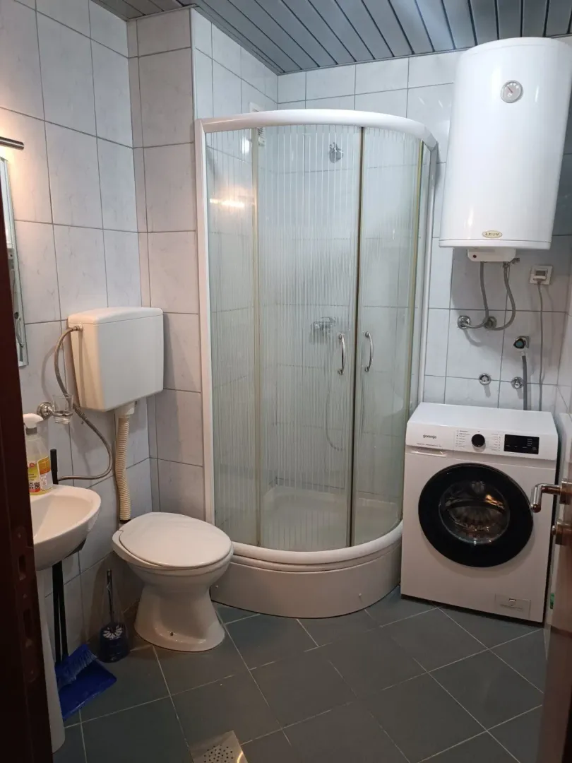 Small bathroom with a shower cabin, toilet, sink, and washing machine.