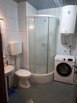 Small bathroom with a shower cabin, toilet, sink, and washing machine. - image 6