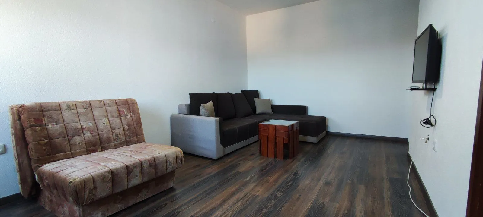 Living room with a corner sofa, an armchair, and a wall-mounted TV.