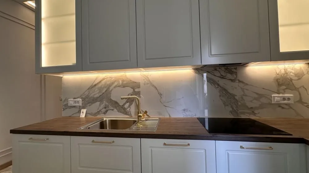 Part of the kitchen featuring a sink, built-in cooktop, and illuminated upper cabinets.