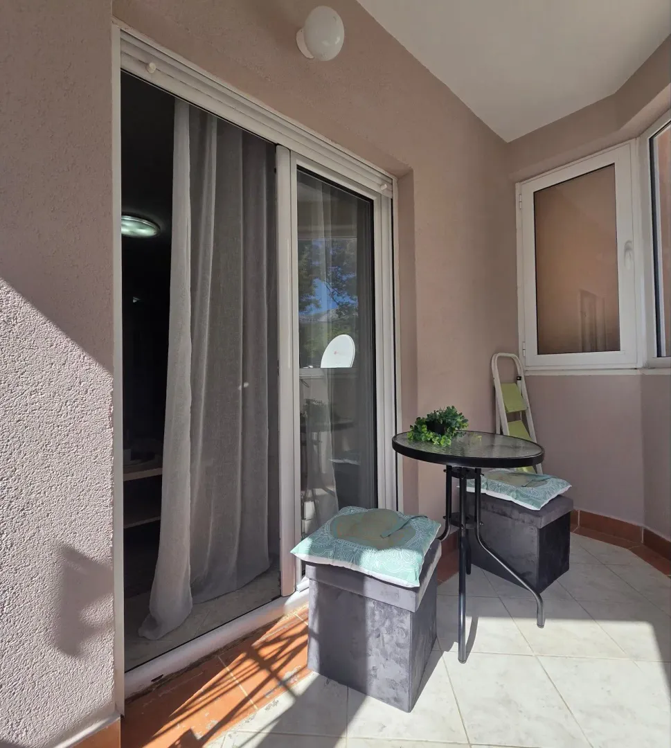 Small furnished balcony area with a glass table and two stools.