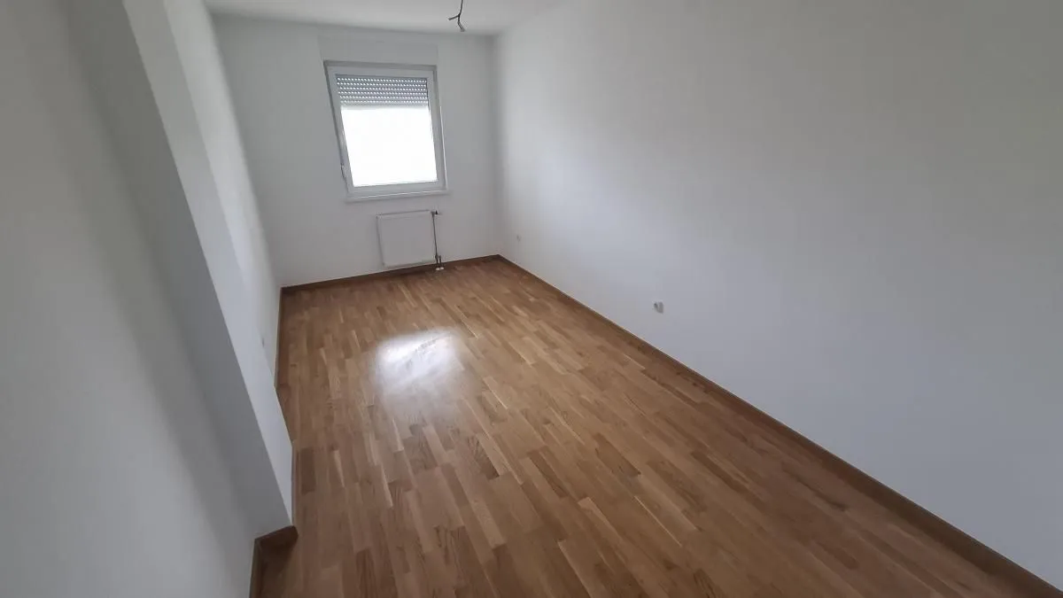 Prazna neopremljena prostorija sa parketom i prozorom.