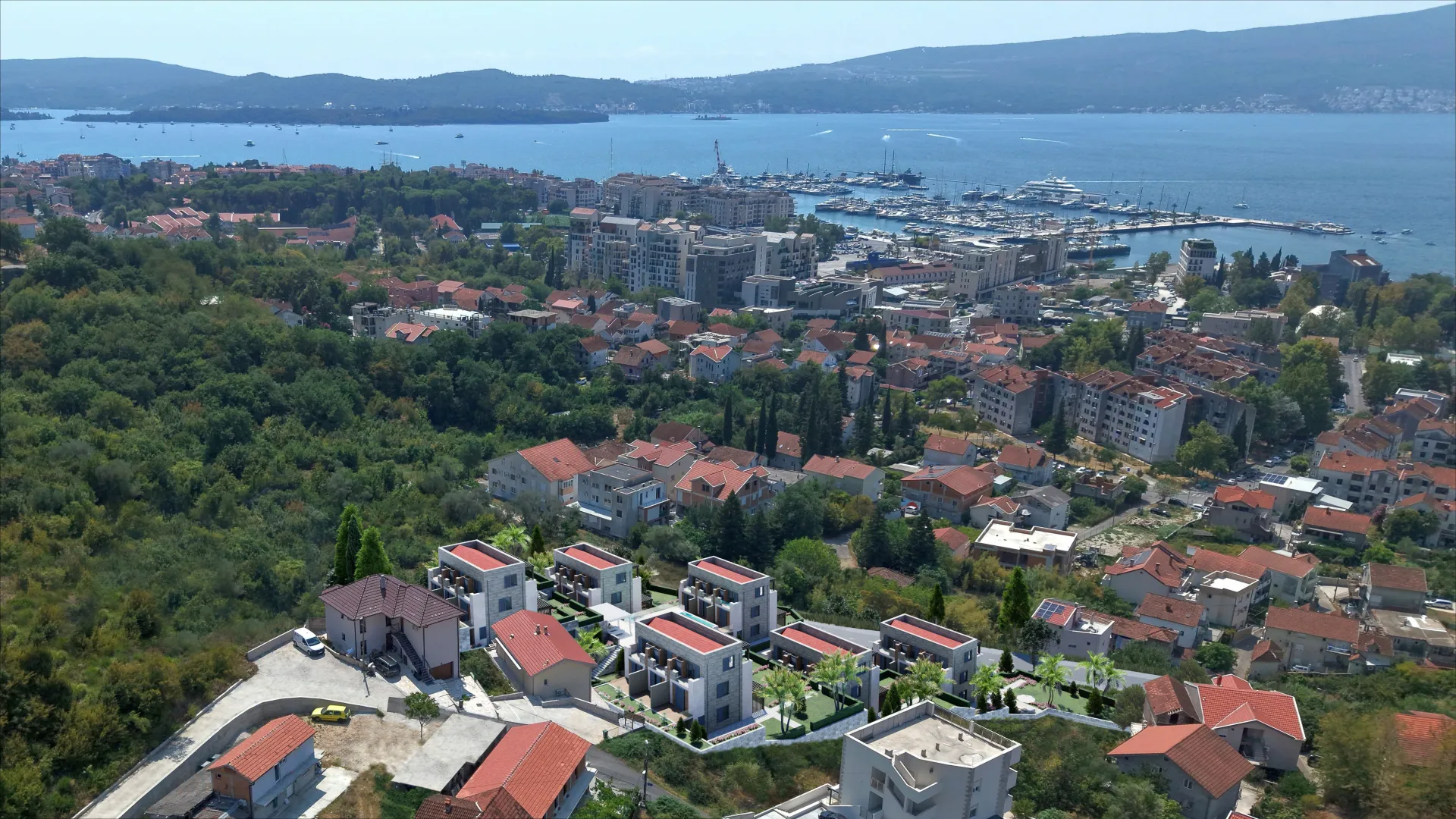 Pogled iz vazduha na kompleks stambenih objekata i grad u pozadini sa pogledom na more.