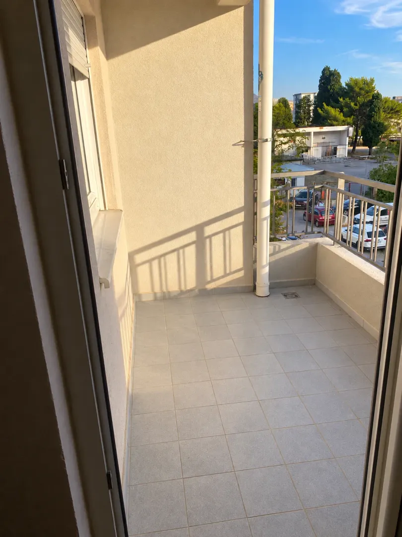 Prazan popločani balkon sa ogradom i pogledom na okolinu.