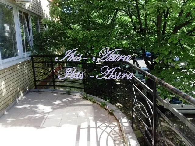 Covered balcony with a metal railing and a view of greenery and parking.