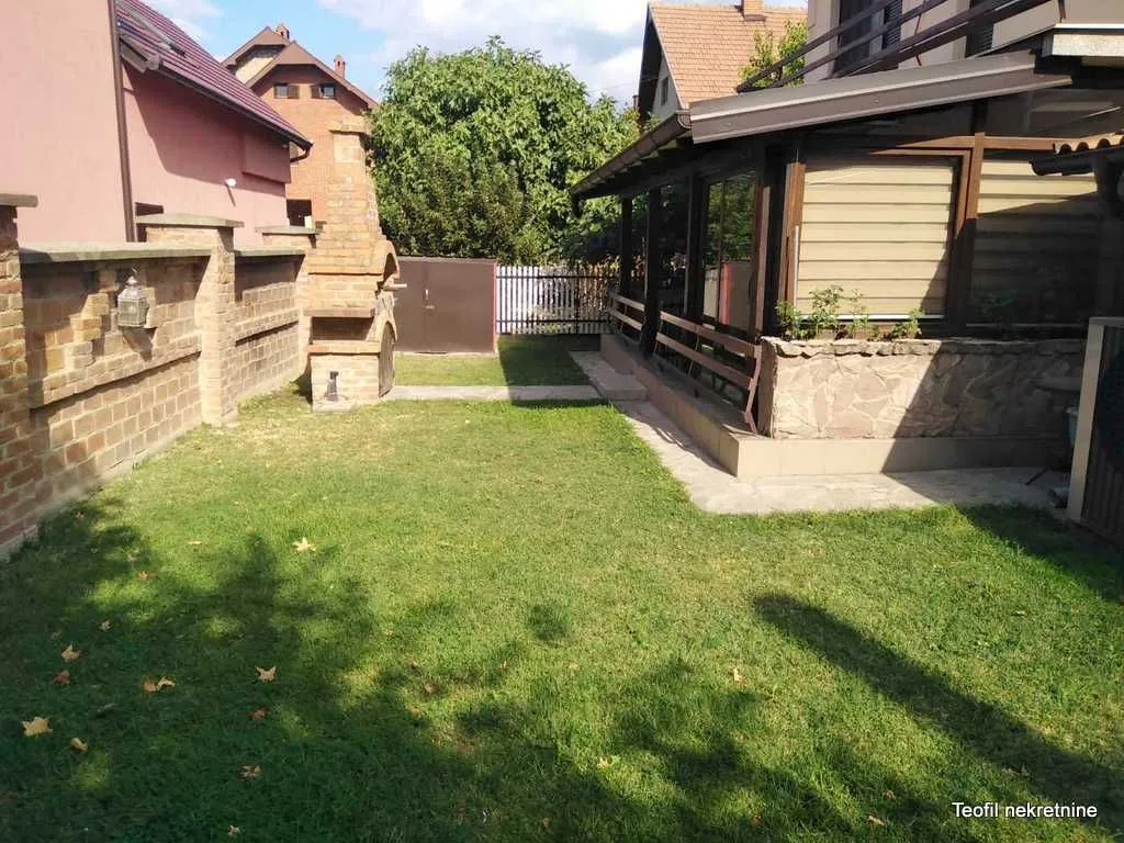 Uređeno dvorište sa travnjakom i zidanim roštiljem pored kuće.