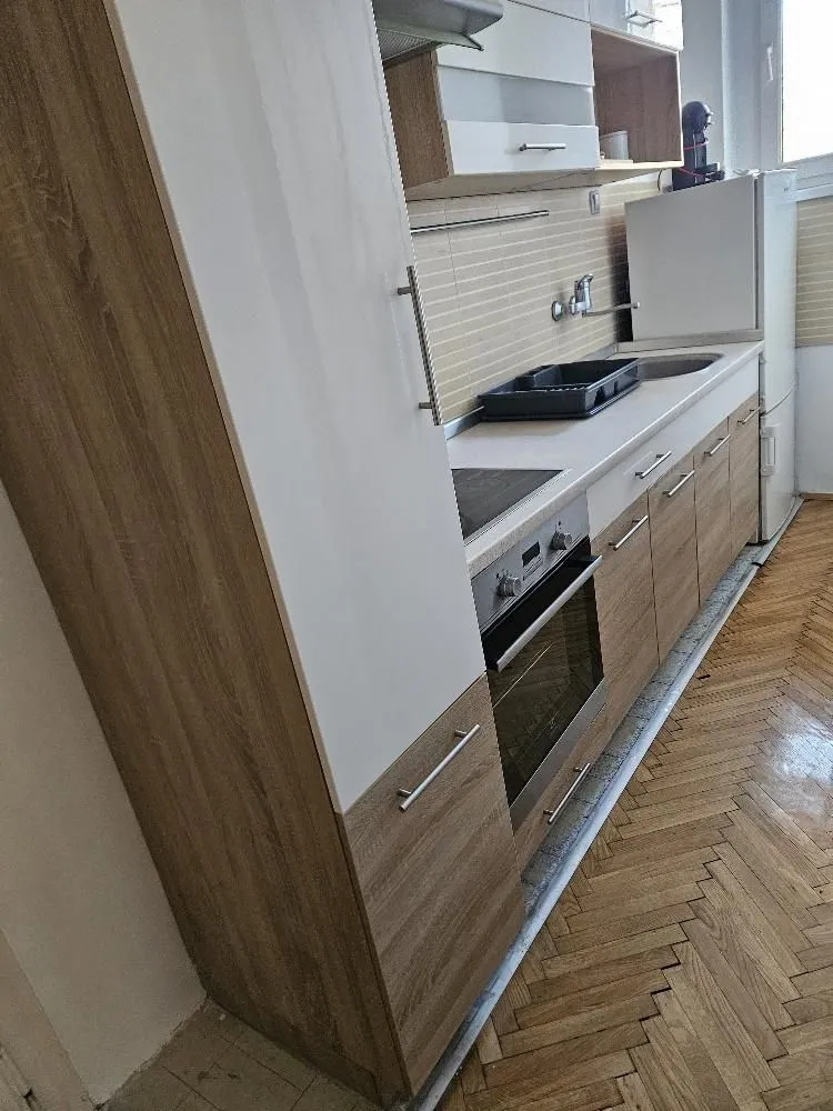 Manja kuhinja sa drvenim elementima, ugradnom rernom i frižiderom.