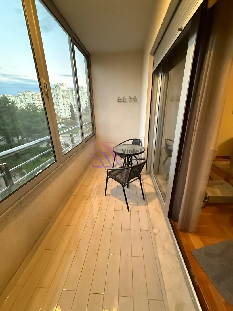 Zastakljeni balkon sa malim stolom, stolicama i pogledom na grad.