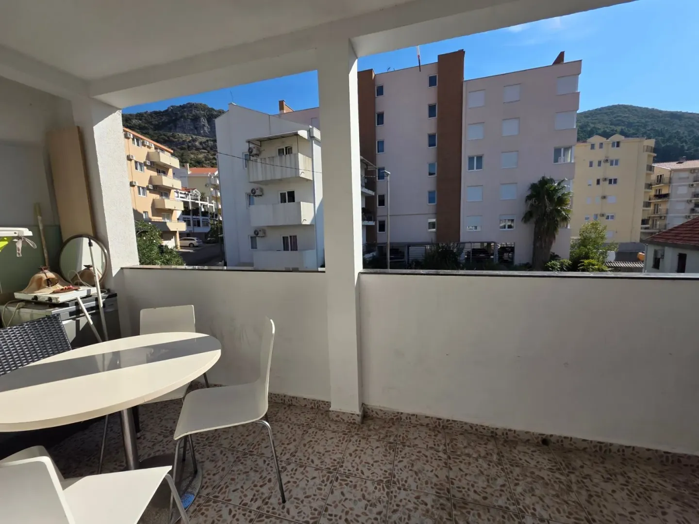 Covered terrace with a table and chairs and a view of surrounding buildings and hills.