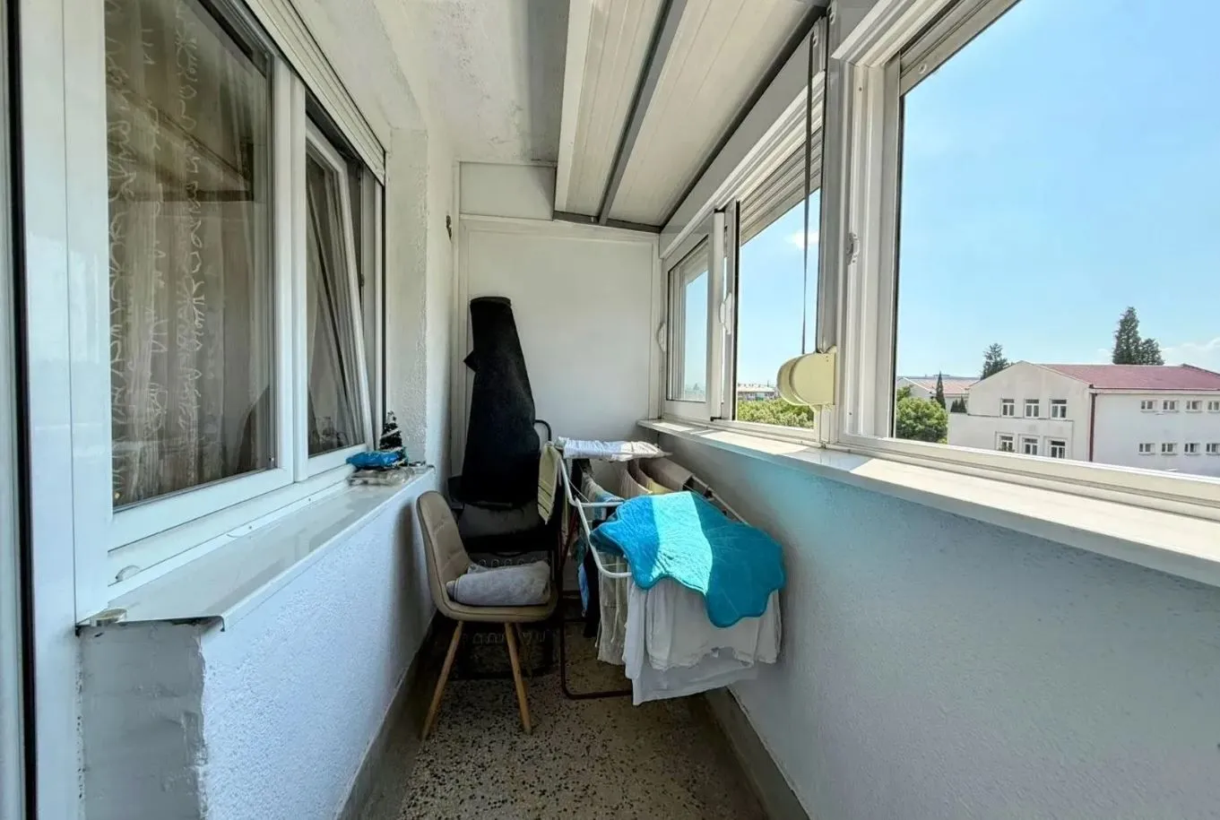 Zastakljeni balkon sa stalcima za sušenje veša i naslaganim stvarima.