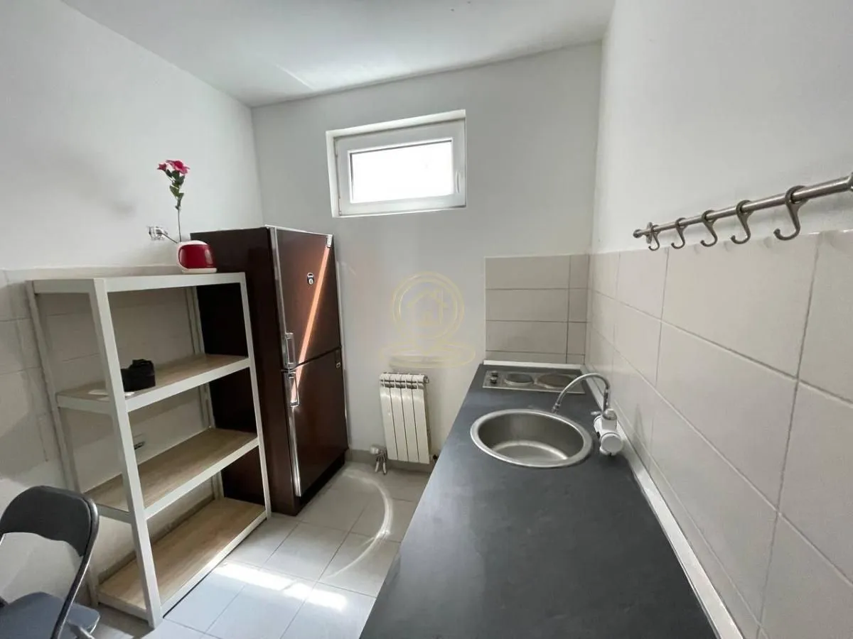Smaller kitchen with refrigerator, sink and shelves.