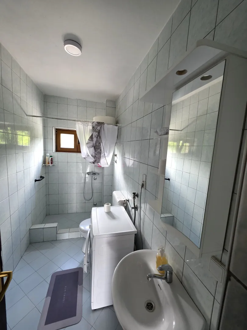 Manje kupatilo obloženo keramičkim pločicama sa tuš kabinom i umivaonikom.