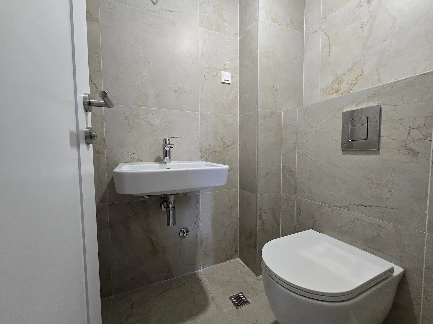 Modernly equipped bathroom with a washbasin and toilet bowl in beige tiles.