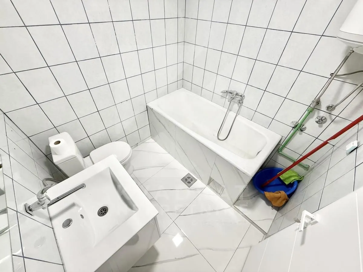 Small bathroom tiled in white with a bathtub, sink, and toilet.