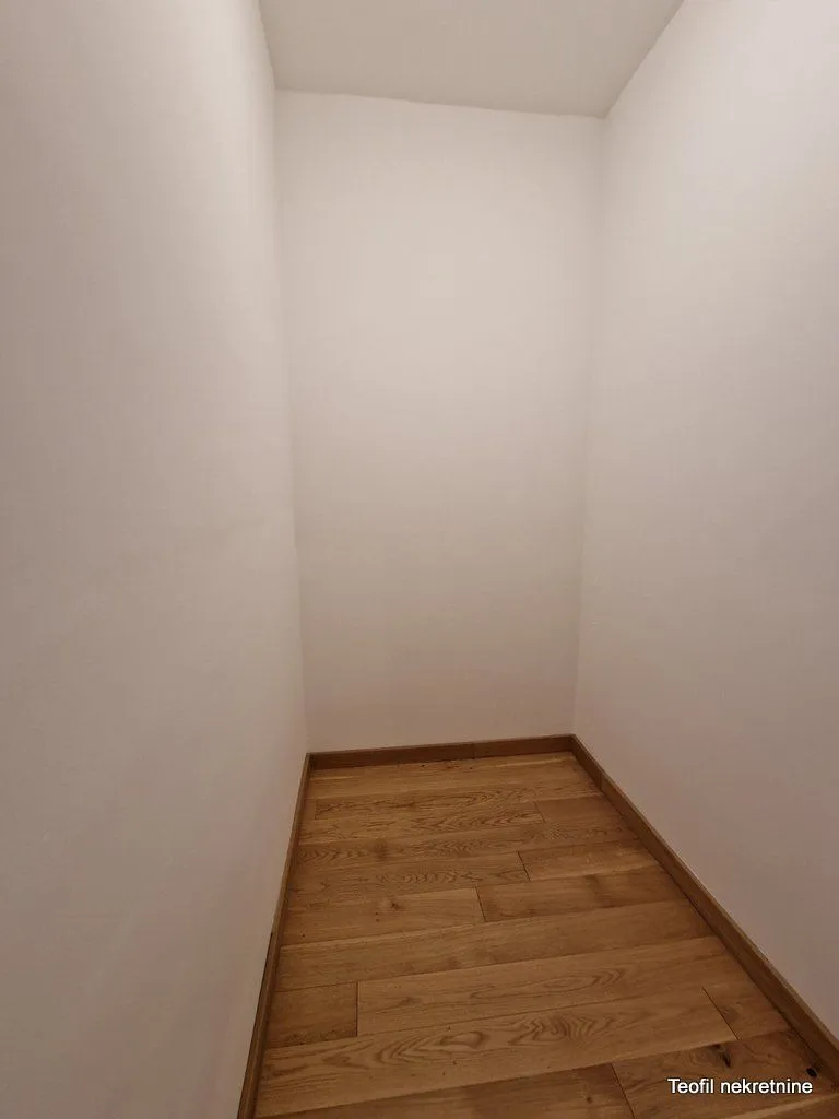 Prazna prostorija sa belim zidovima i drvenim podom.