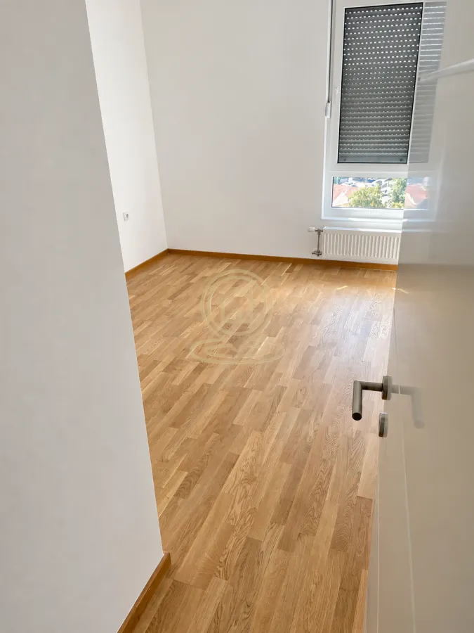 Prazna soba sa drvenim parketom i prozorom.
