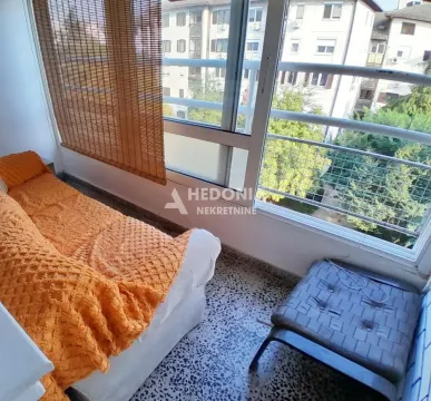 Zastakljeni balkon sa garniturom za sedenje i pogledom na okolne zgrade. - image 2