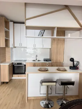 Moderna kuhinja sa bijelim elementima, drvenim detaljima i šankom sa barskim stolicama. - image 5