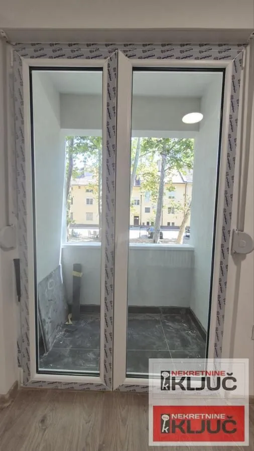 Pogled kroz balkonska vrata na terasu i okolne zgrade.