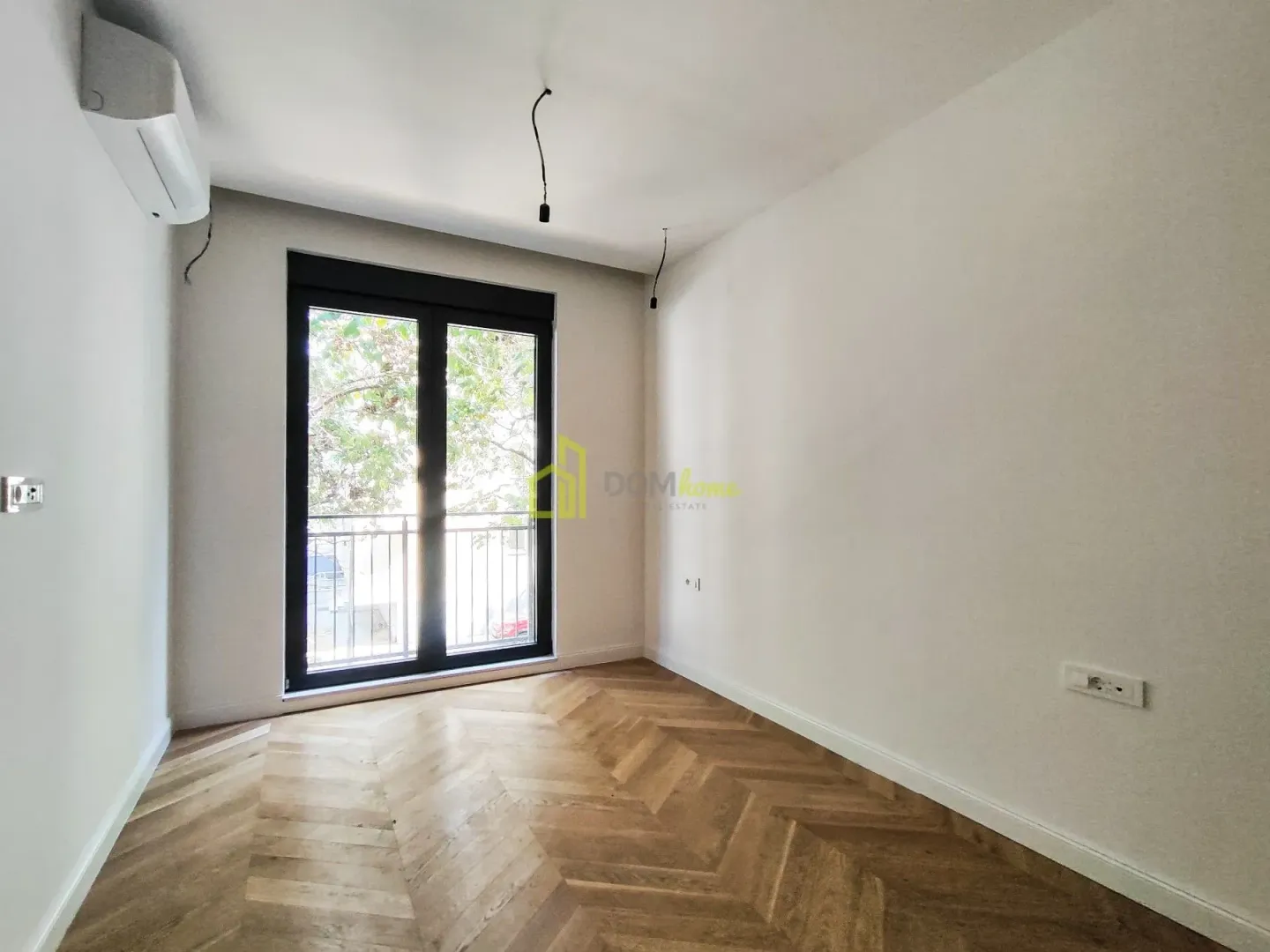 Prazna soba sa drvenim podom i izlazom na balkon.