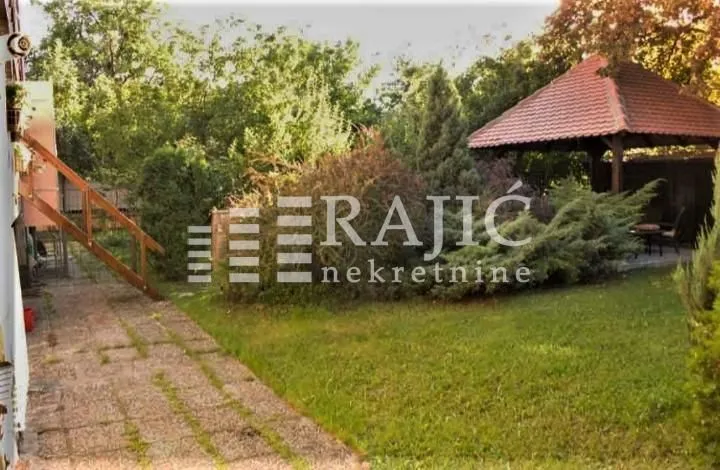 Uređeno dvorište sa travnjakom, drvećem i nadstrešnicom.