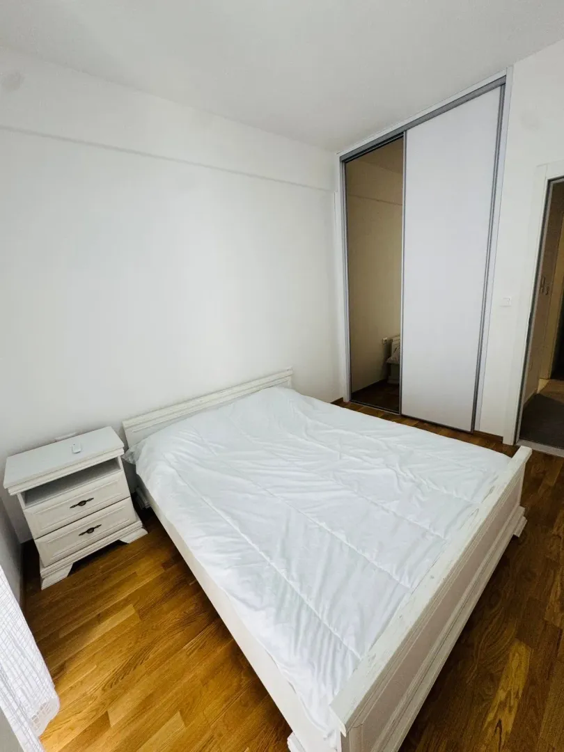 Bright bedroom with a white bed, nightstand, and built-in closet.
