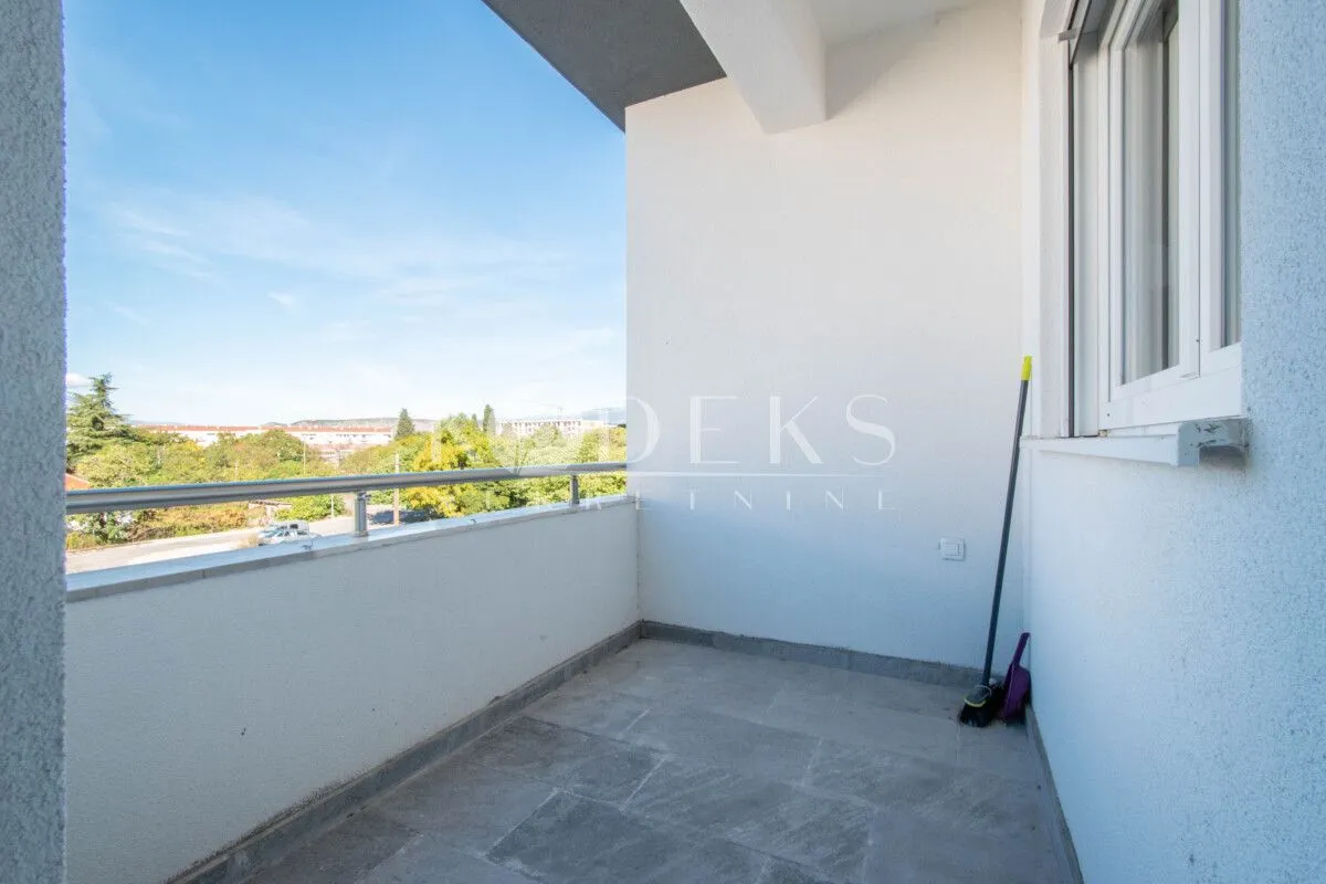 Nenamešten balkon sa metalnom ogradom i pogledom na okolinu.