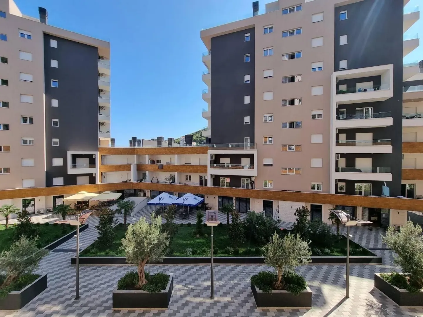 Moderni stambeni kompleks sa uređenim dvorištem i popločanim stazama.