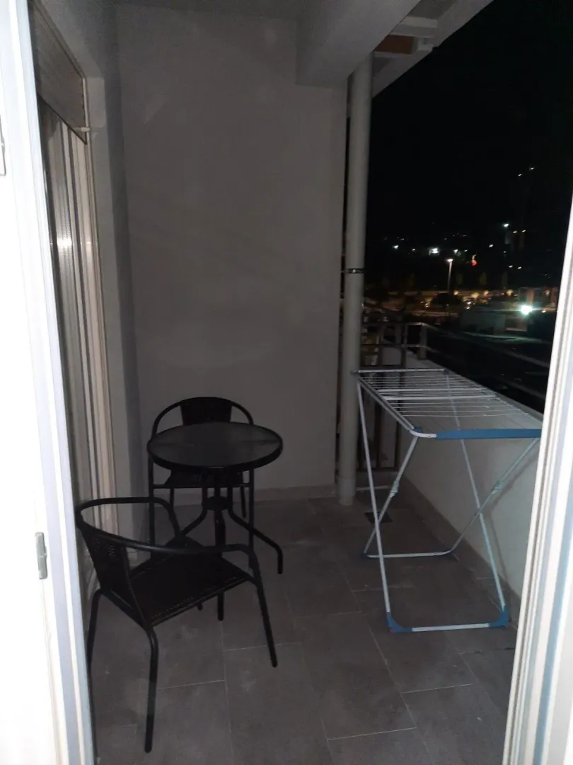 A balcony featuring a small table, two chairs, and a clothes drying rack at night.