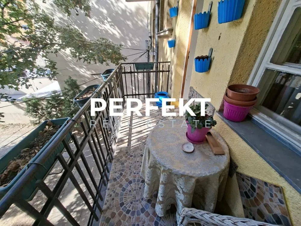 Manji namešten balkon sa stolom, stolicom i ukrasnim saksijama za cveće.