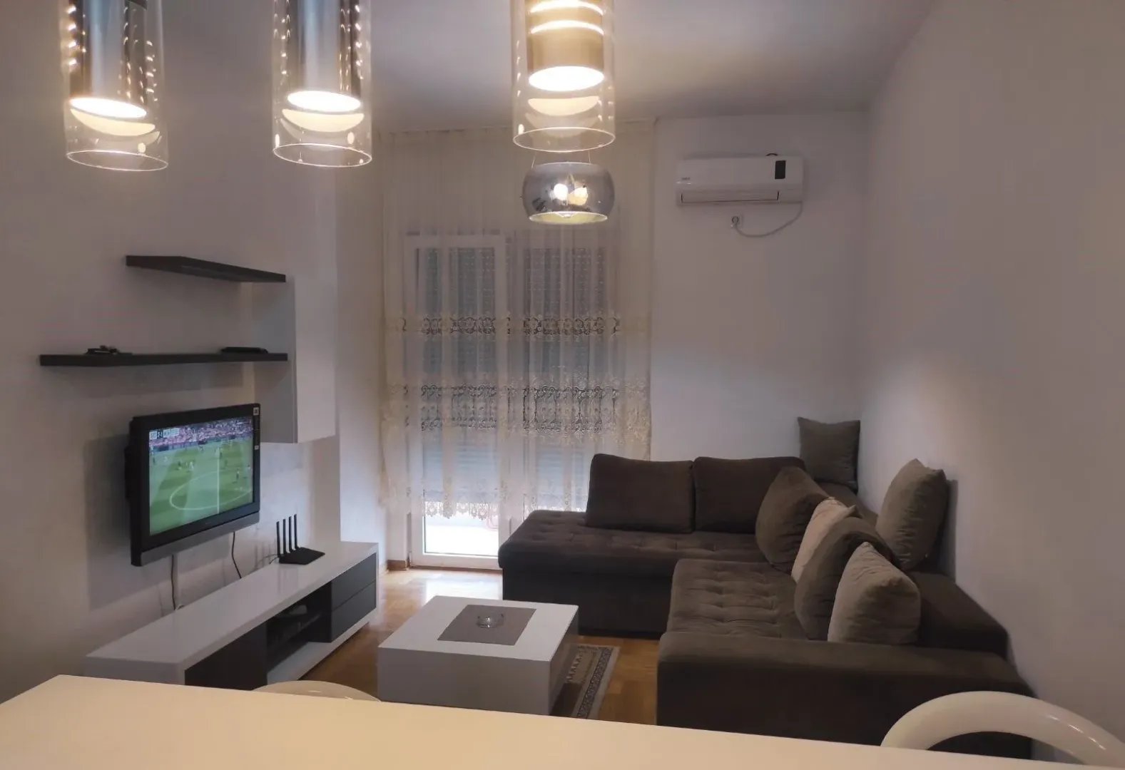 Living room with a sectional sofa, TV, and modern lighting.