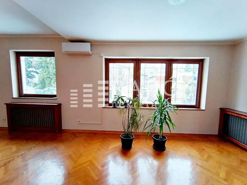 Spacious empty room with wooden flooring and large windows.