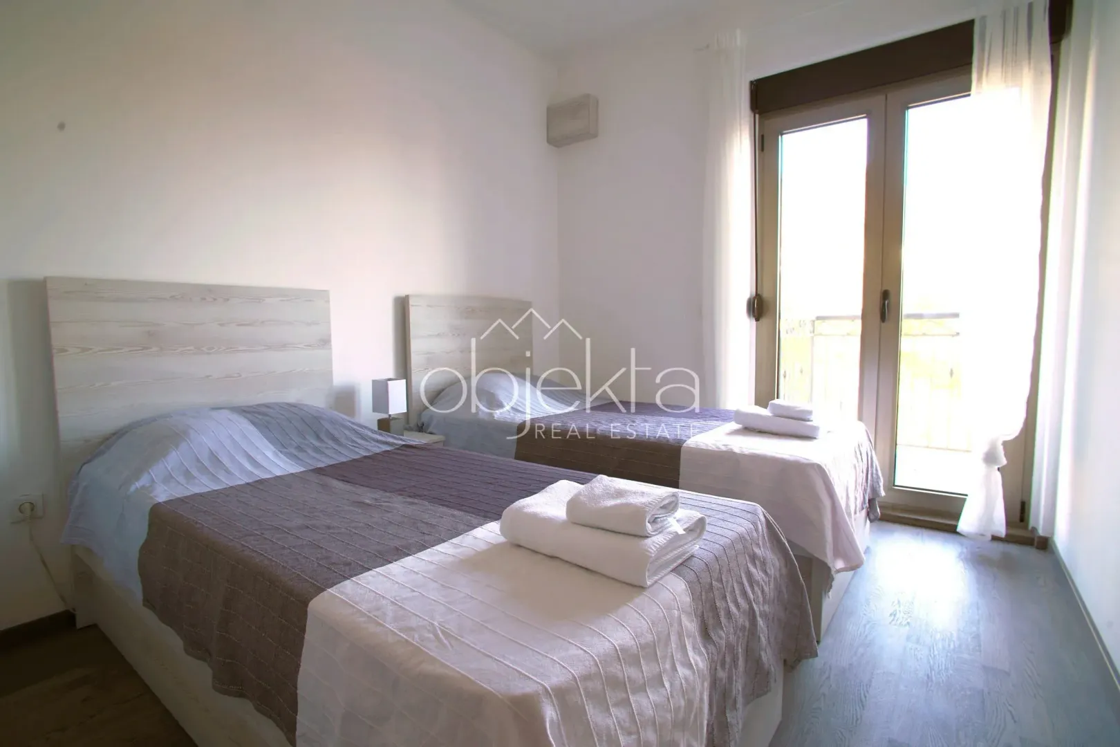 Spavaća soba sa dva odvojena kreveta i balkonskim vratima.