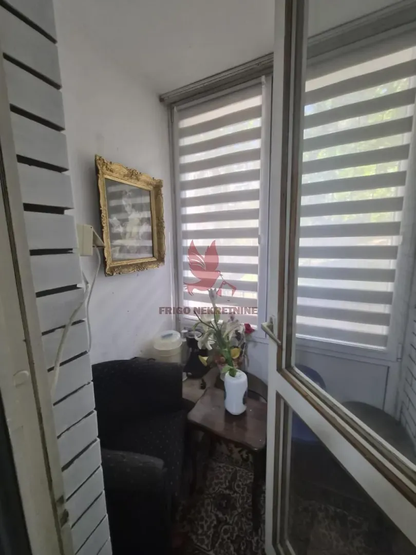 Zastakljena terasa sa garniturom za sedenje i roletnama na prozorima.