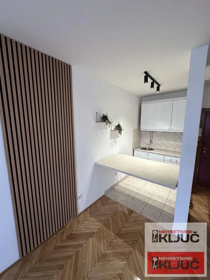 Manja kuhinja sa belim elementima i šankom povezana sa trpezarijom.