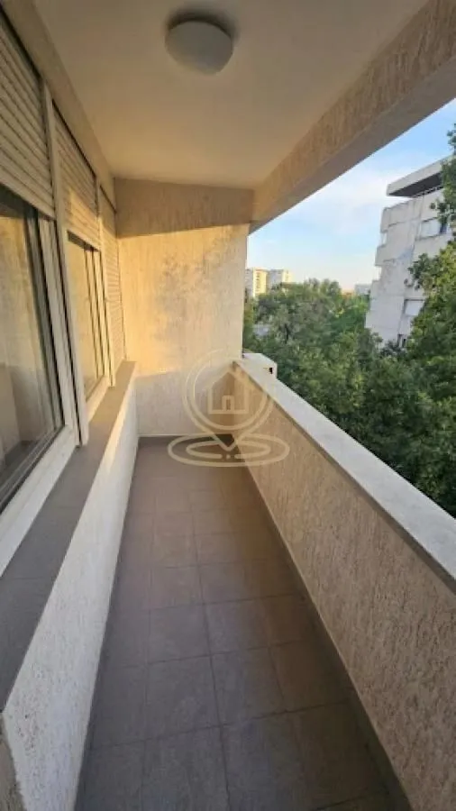 Long covered balcony with a view of greenery and surrounding buildings.
