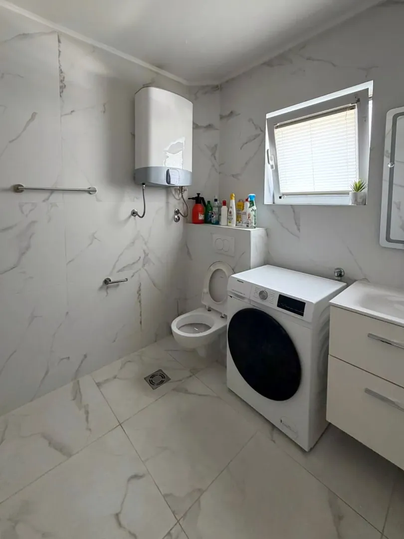 Kupatilo sa veš mašinom, WC šoljom, umivaonikom i bojlerom na zidu.