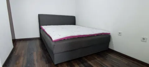 A simply furnished bedroom with a grey double bed and dark laminate flooring. - image 16