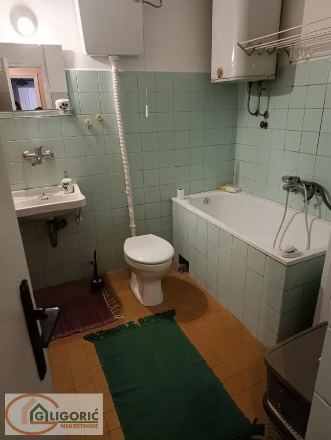 Kupatilo sa kadom, umivaonikom i toaletom obloženo zelenim pločicama.