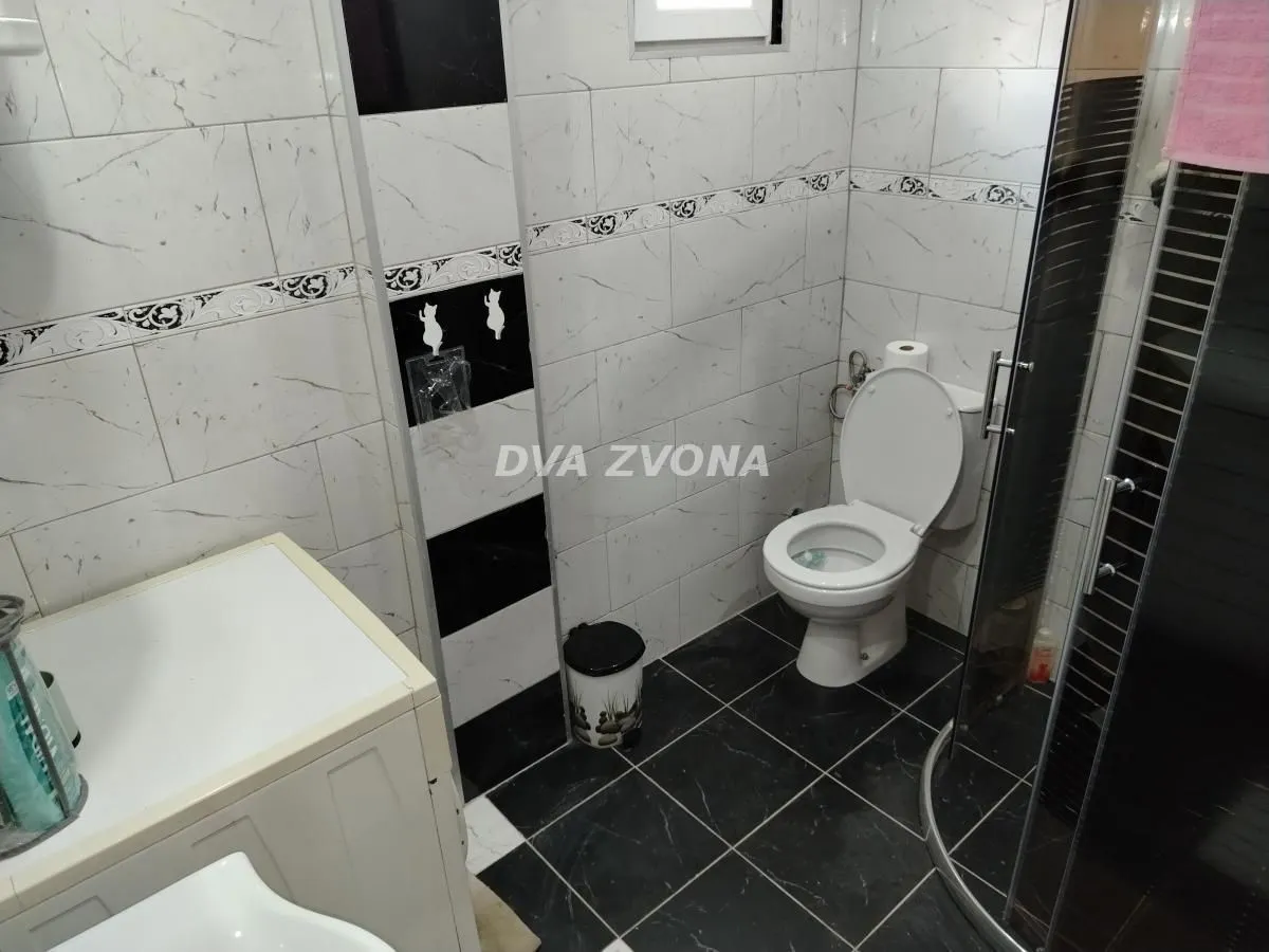 Manje kupatilo sa tuš kabinom, belim pločicama i sanitarijama.