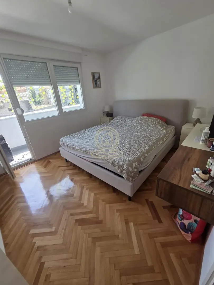 Spavaća soba sa bračnim krevetom, drvenim parketom i izlazom na terasu.