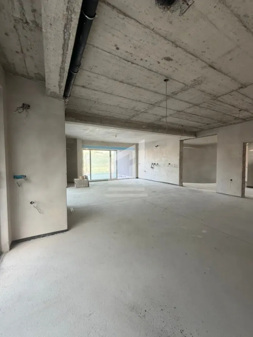Pogled na nenamješten prostor u izgradnji sa betonskim plafonom i grubim zidovima.