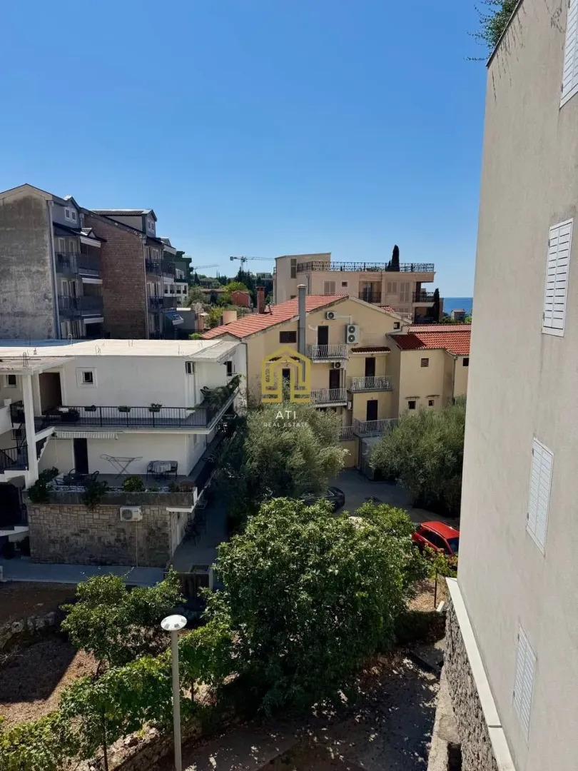 View from the terrace of surrounding buildings, greenery, and the sea in the distance.