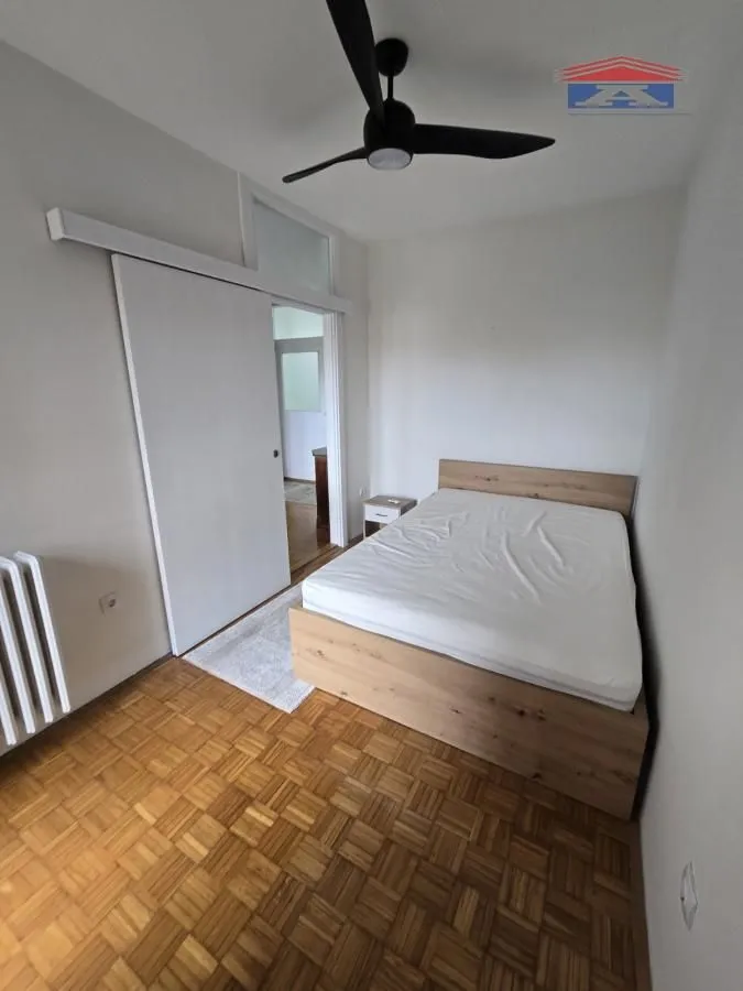 Spavaća soba sa bračnim krevetom, drvenim parketom i plafonskim ventilatorom.