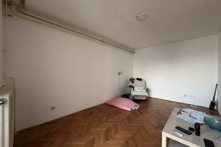 Prazna soba sa parketom na podu i vidljivim instalacijama na zidu.