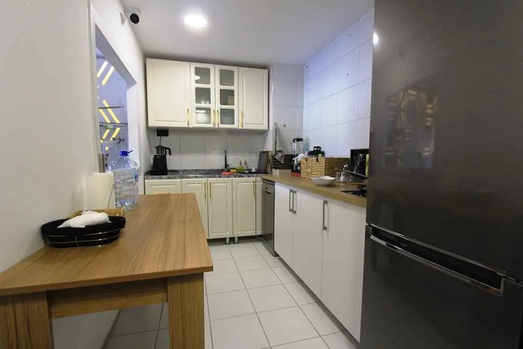 Small kitchen with white cabinets, a wooden dining table, and a refrigerator.
