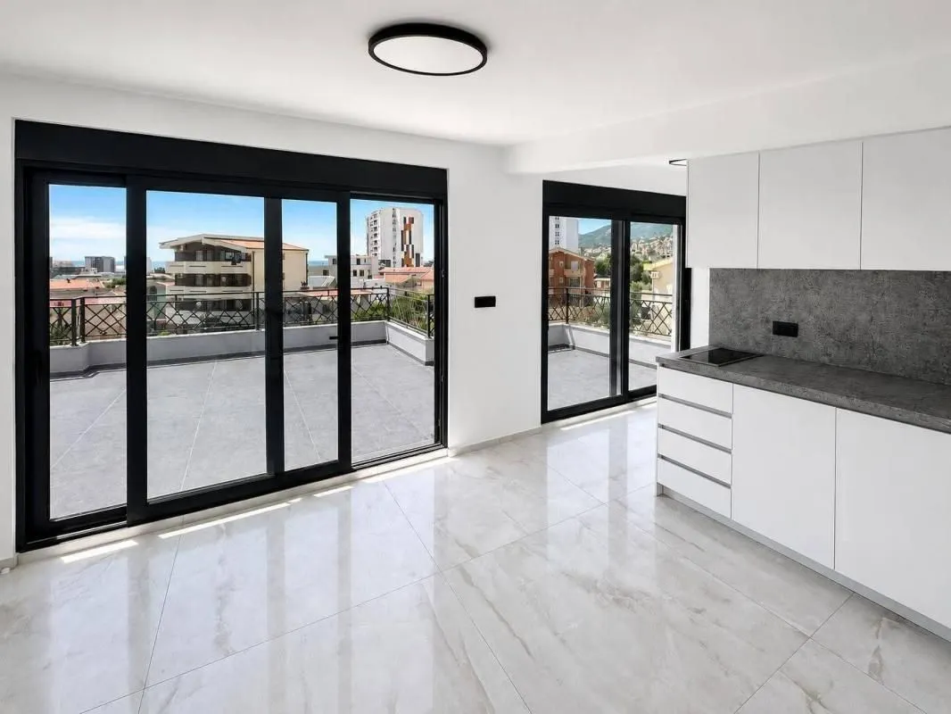 Living room with a kitchen and large glass surfaces leading to the terrace.