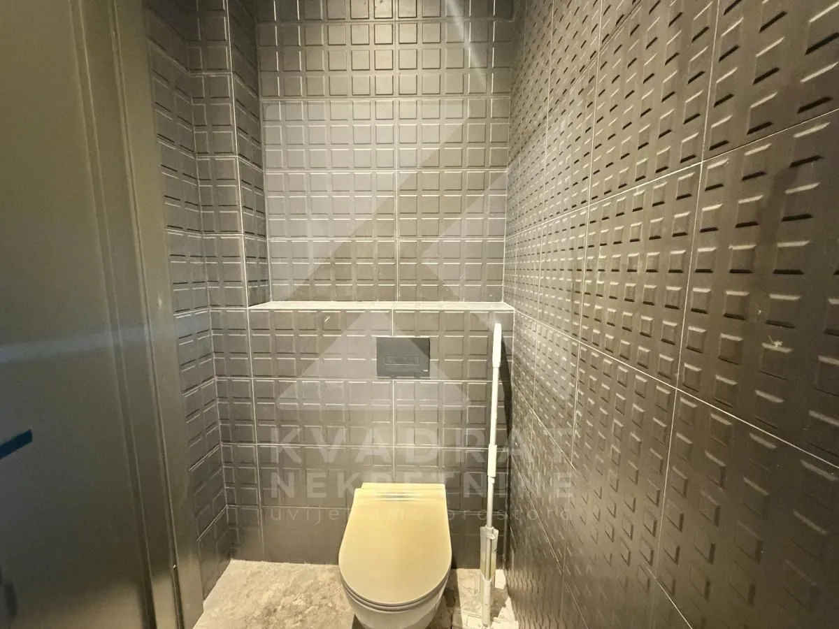 Modern bathroom with dark tiles and a wall-mounted toilet.